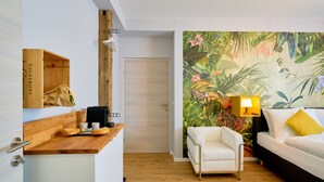A modern room with a wooden desk, a white sofa, a white armchair, and a vibrant tropical mural on the wall. - Leuhusen Center Apartments Vienna (Vienna)