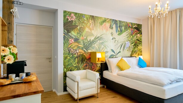 A hotel room with a bed, a chair, a desk with a lamp, and a tropical-themed wall mural. - Leuhusen Center Apartments Vienna (Vienna)