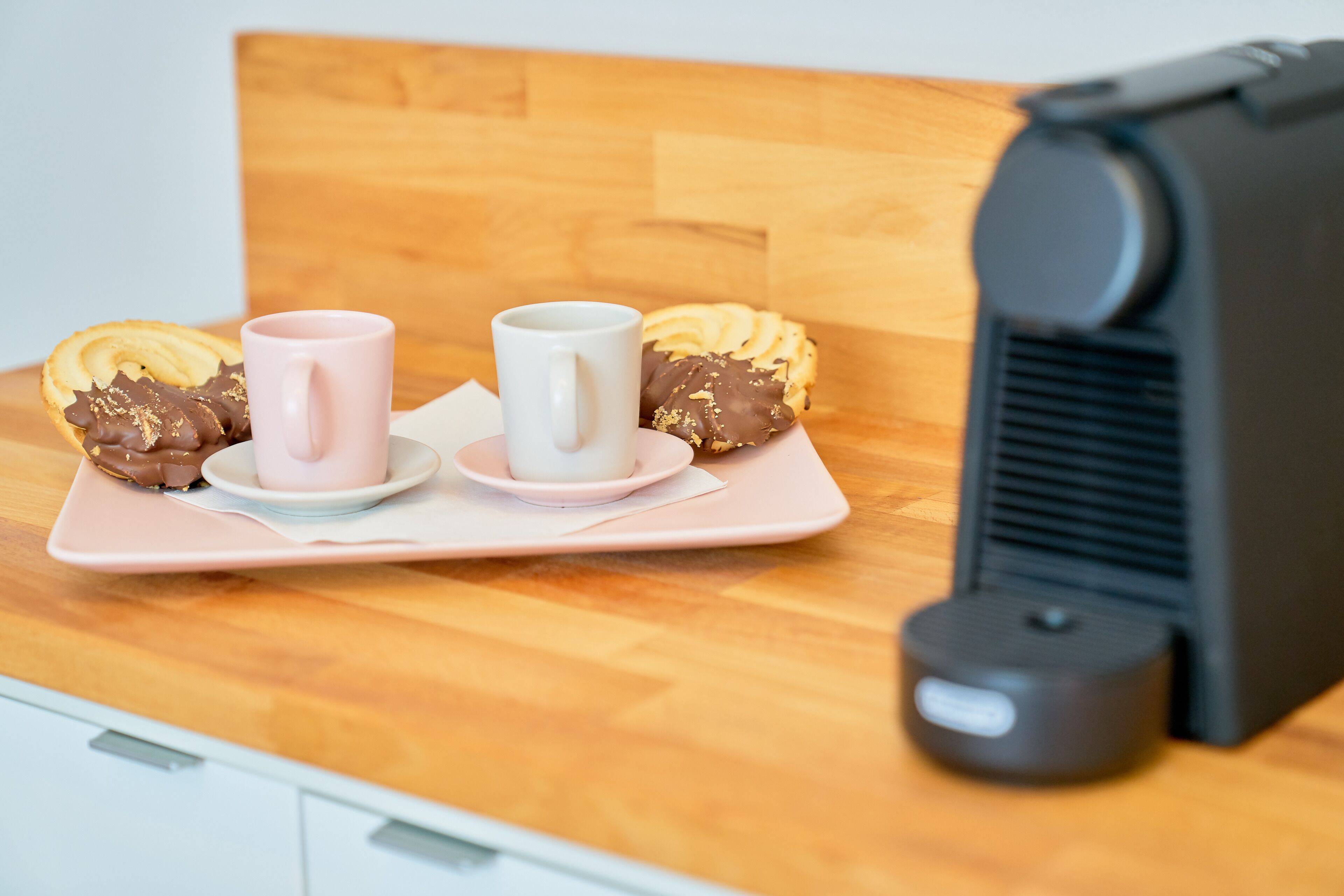 Bandeja de desayuno con pasteles y dos tazas sobre una mesa de madera junto a una cafetera.
