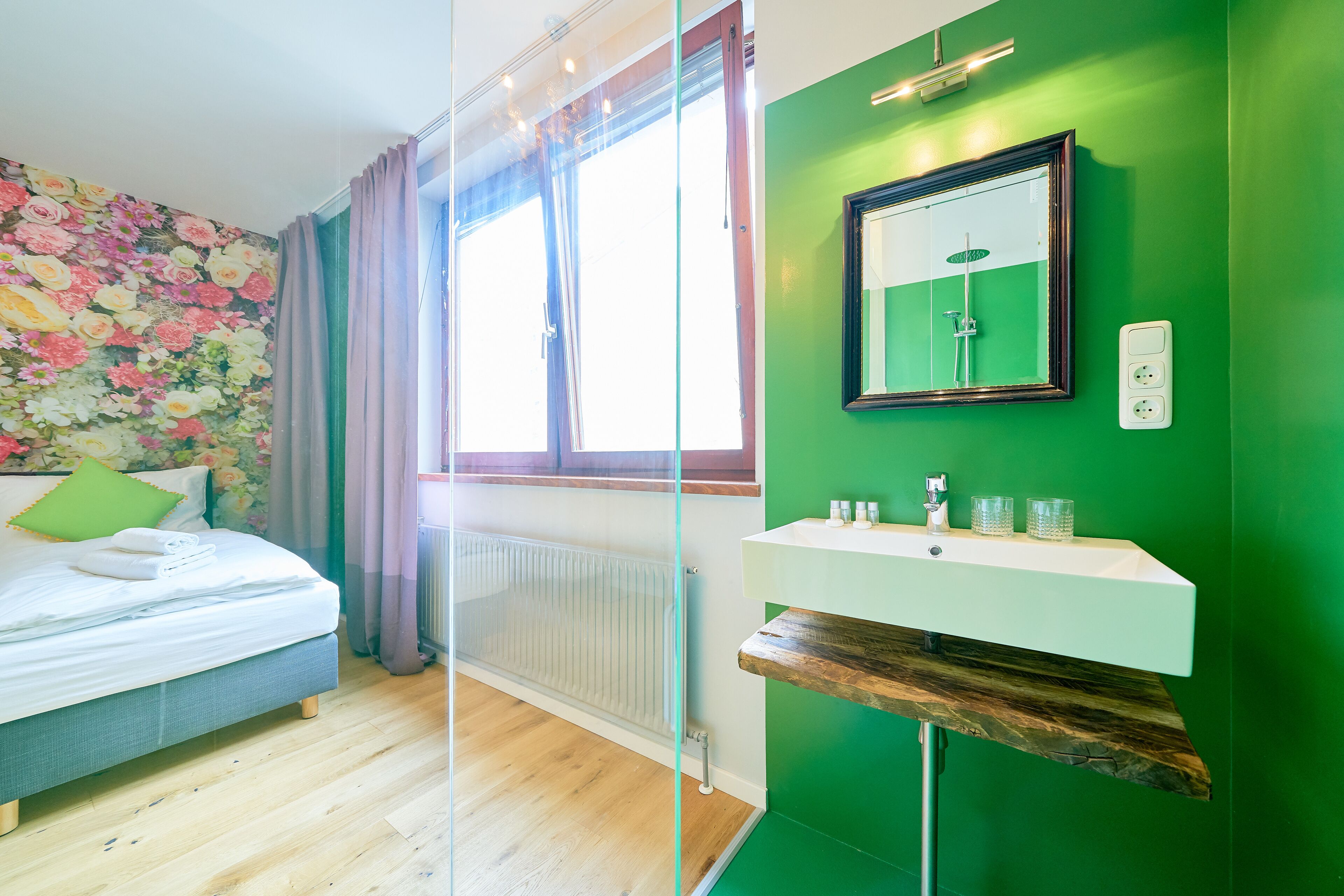 Une chambre moderne avec un lit, un mur vert, une fenêtre avec des rideaux et une salle de bain avec un miroir et un lavabo.