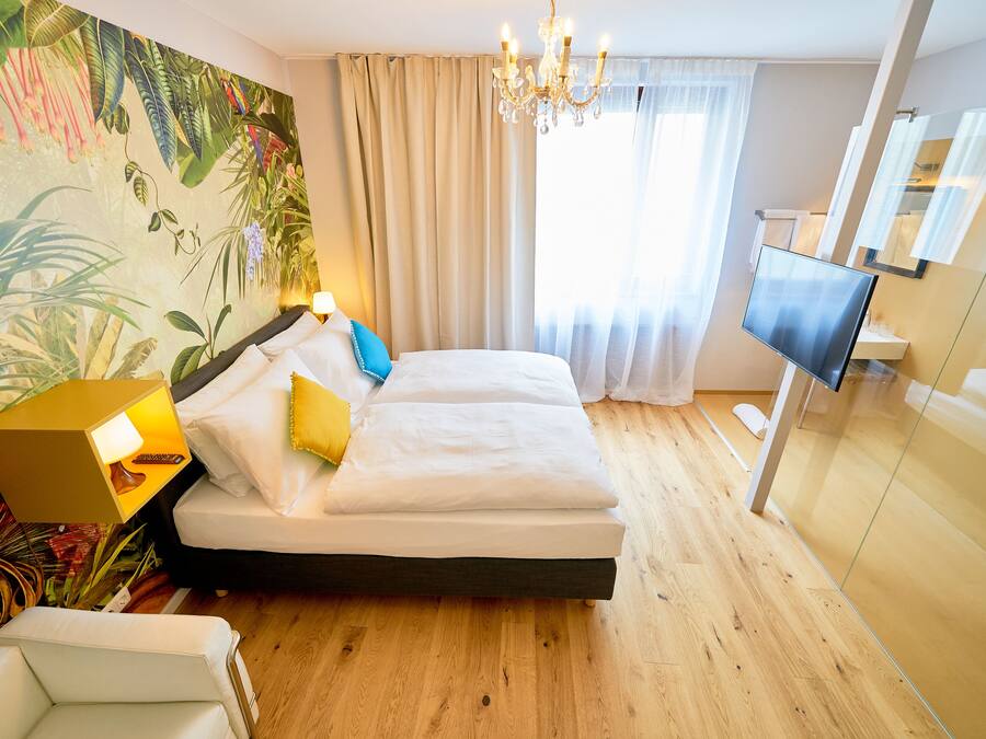 Una habitación de hotel con cama, televisión, candelabro y una pared cubierta de plantas.