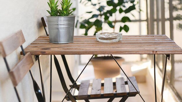 Une table en bois avec des pieds en métal, un seau en métal et une plante en pot sur un balcon.