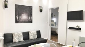 Un salon moderne avec un canapé en cuir noir, une table basse ronde et un téléviseur à écran plat fixé au mur.