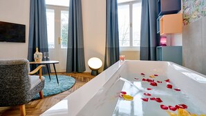 A modern bathroom with a bathtub filled with rose petals, a small round table with a lamp, and a chair.