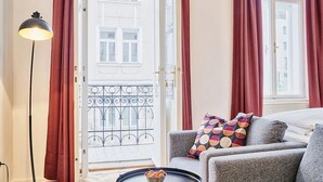 A room with a bed, a grey sofa, a floor lamp, and a view of a balcony with metal railings.