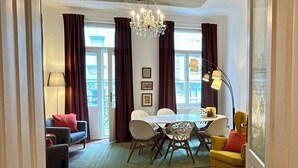 A dining area with a chandelier, a table with chairs, and a view through large windows.