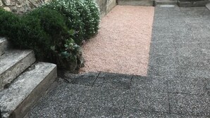 Een binnenplaats met stenen trappen die leiden naar een grindpad, omgeven door groen en een stenen muur.
