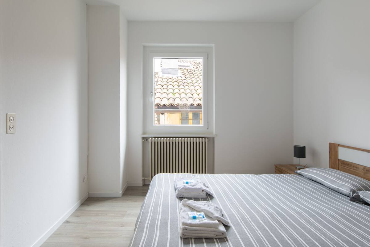 Ein Schlafzimmer mit Bett, Fenster, Heizkörper und Nachttisch mit Lampe.