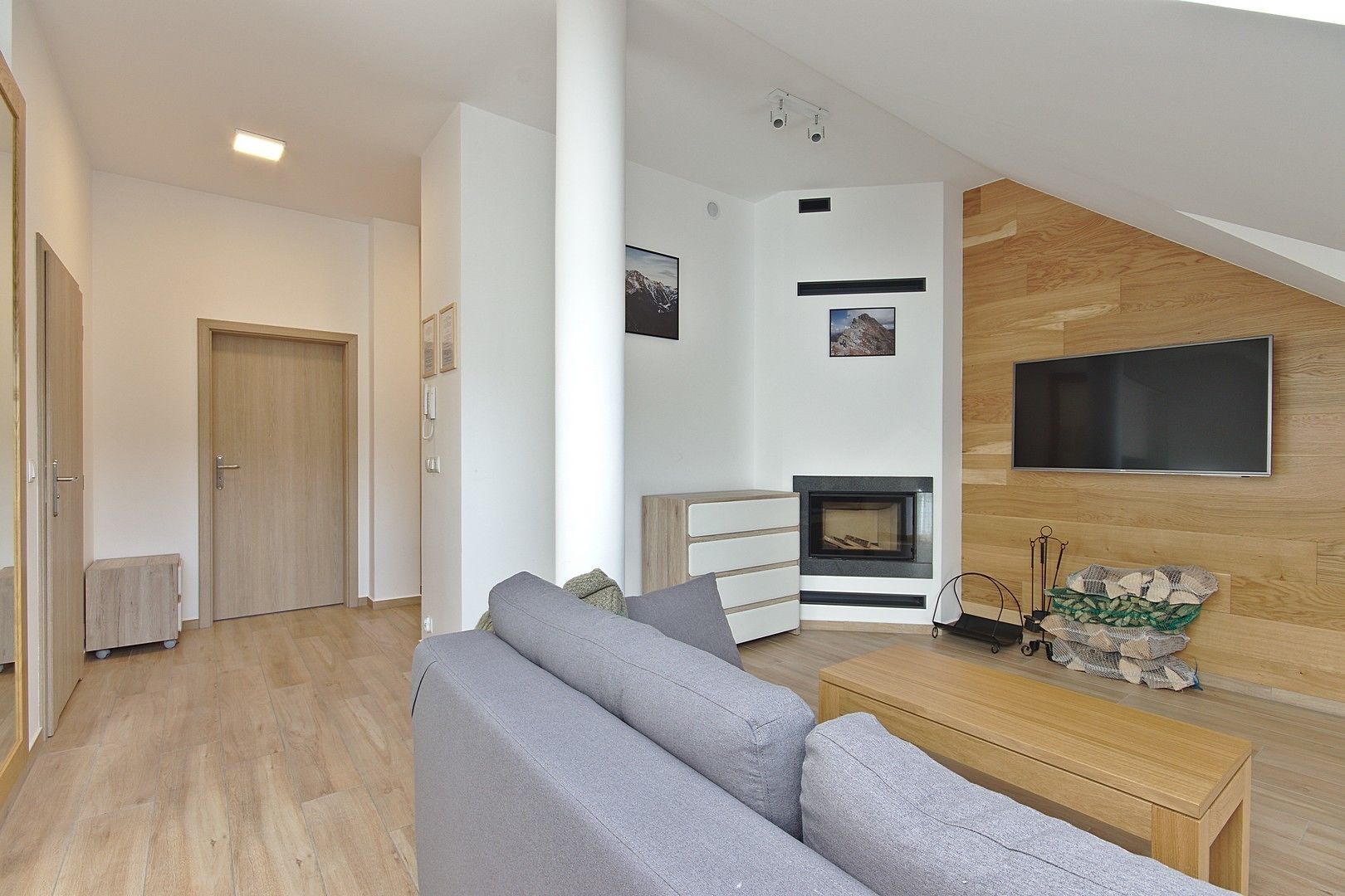 A modern living room with a fireplace, a flat-screen TV mounted on the wall, and a wooden bench.