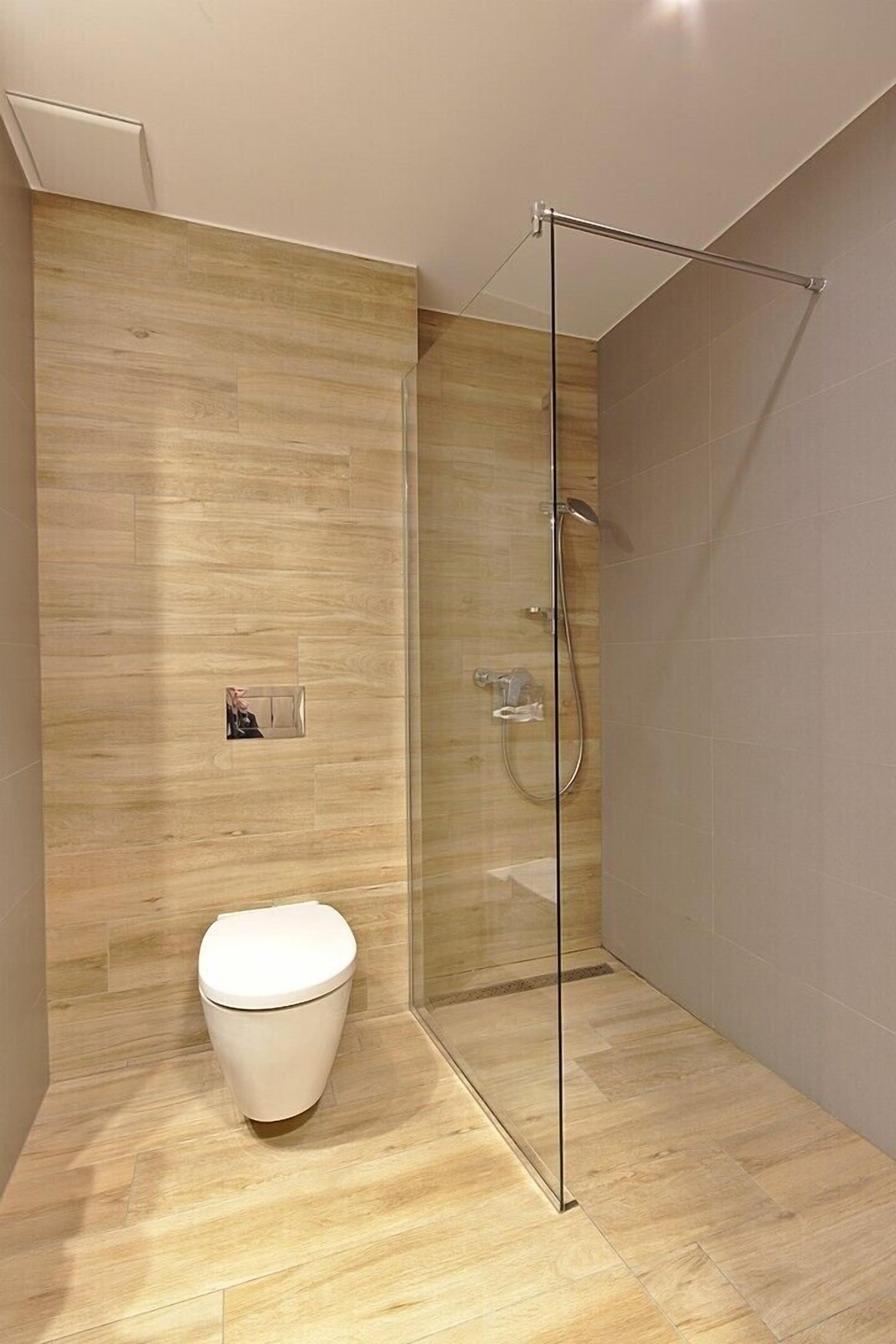 Un baño moderno con cabina de ducha de vidrio, inodoro blanco y suelo de madera.