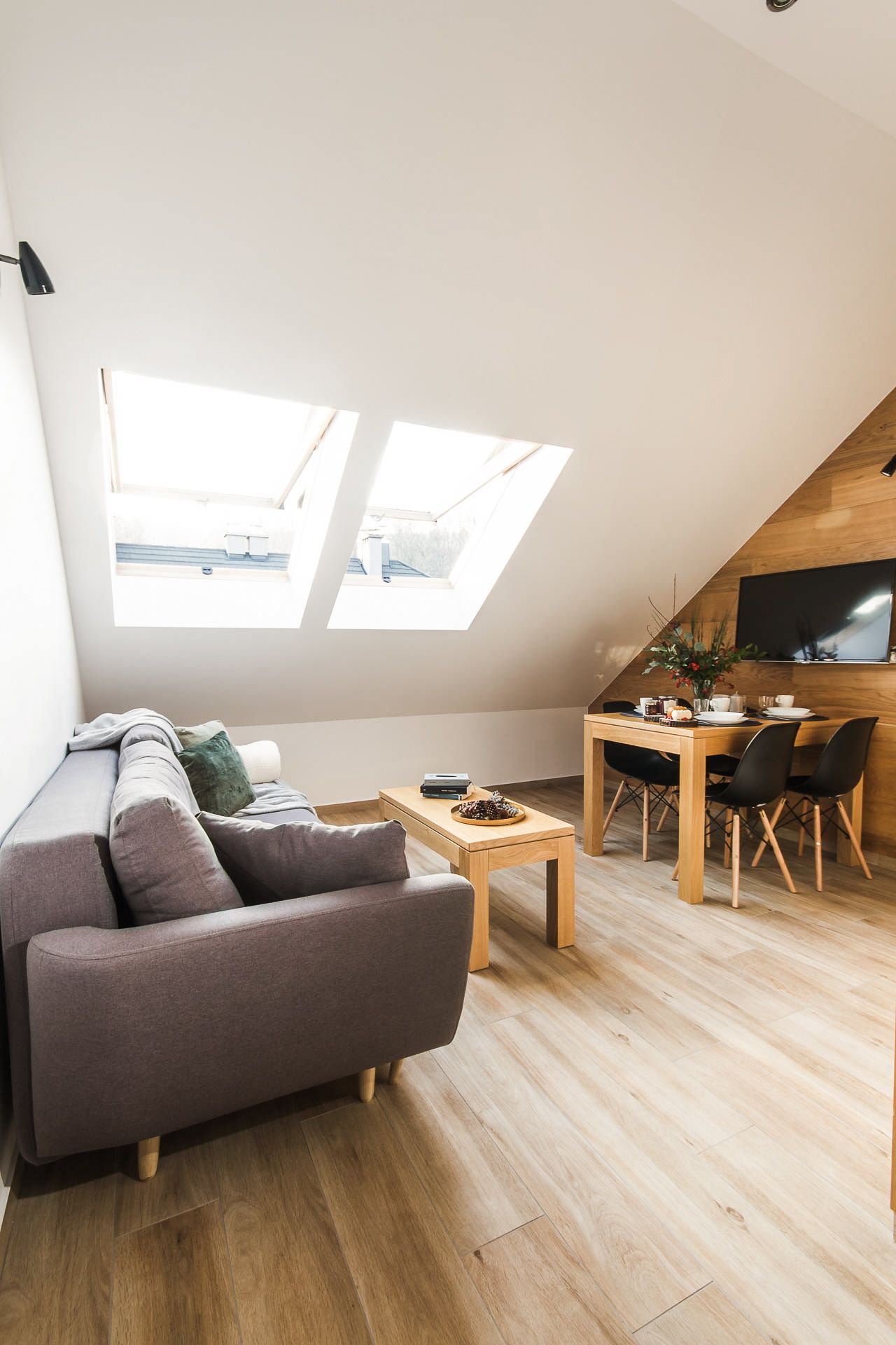 Un moderno apartamento tipo loft con cama de altillo, comedor con mesa y sillas de madera, y tragaluces que aportan luz natural.