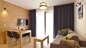 Un salon moderne avec un mur en bois, un canapé avec des coussins, une table à manger avec des chaises, un téléviseur fixé au mur et une grande fenêtre avec des rideaux.