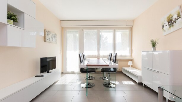 A modern kitchen with a dining table, chairs, a TV, and a refrigerator. - Girasole (Savosa)