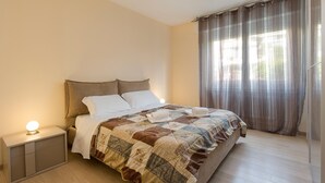 A neatly made bed with a quilt, a bedside table with a lamp, and a window with curtains. - Girasole (Savosa)