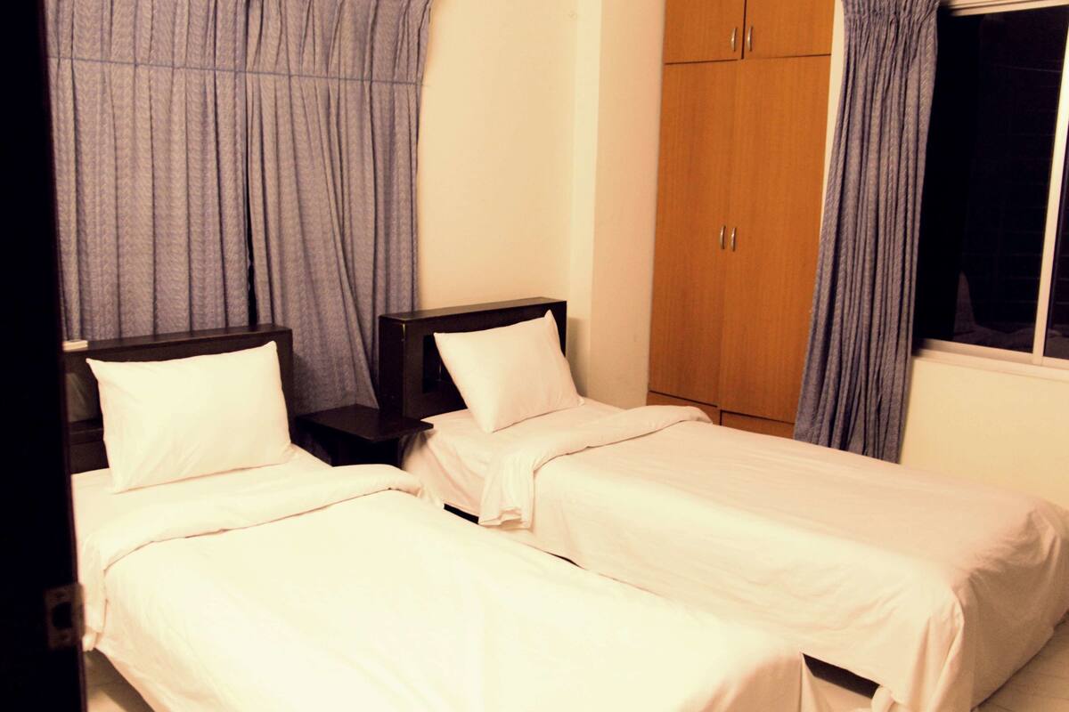 A room with two single beds, a wooden wardrobe, and a window with curtains.