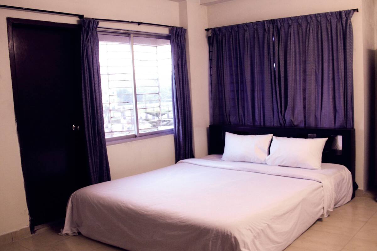 A hotel room with a bed, a window with curtains, and a door.