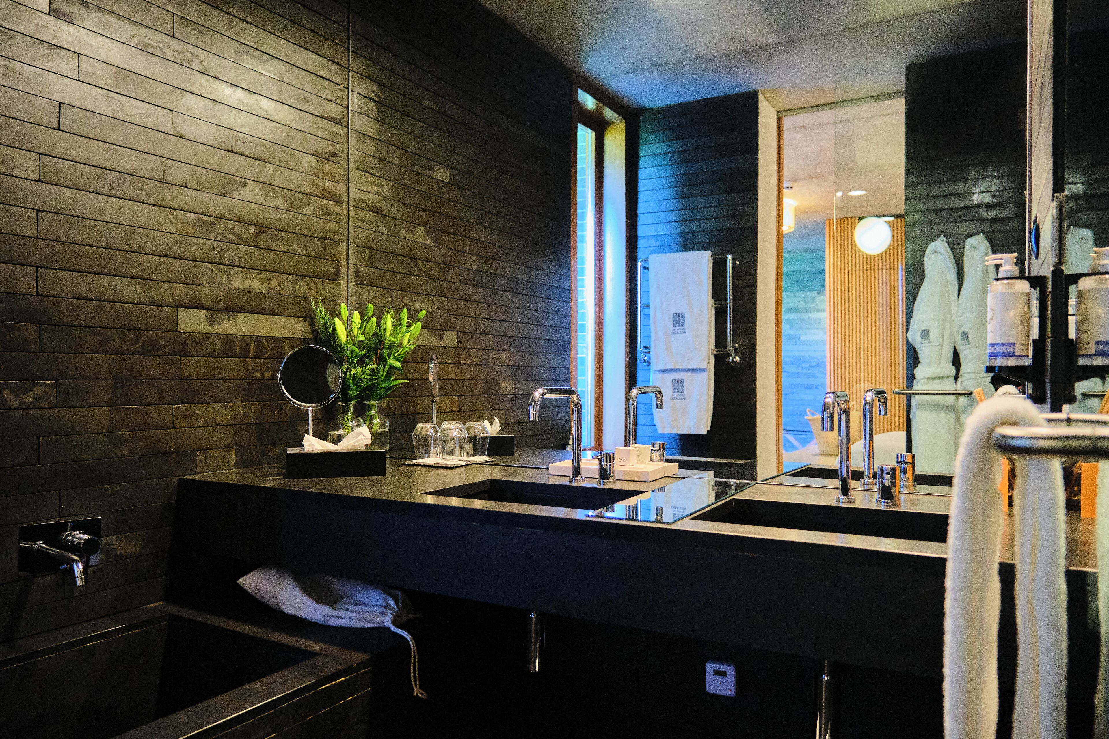 Un baño moderno con pared de madera, lavamanos dobles, espejo y toallero.