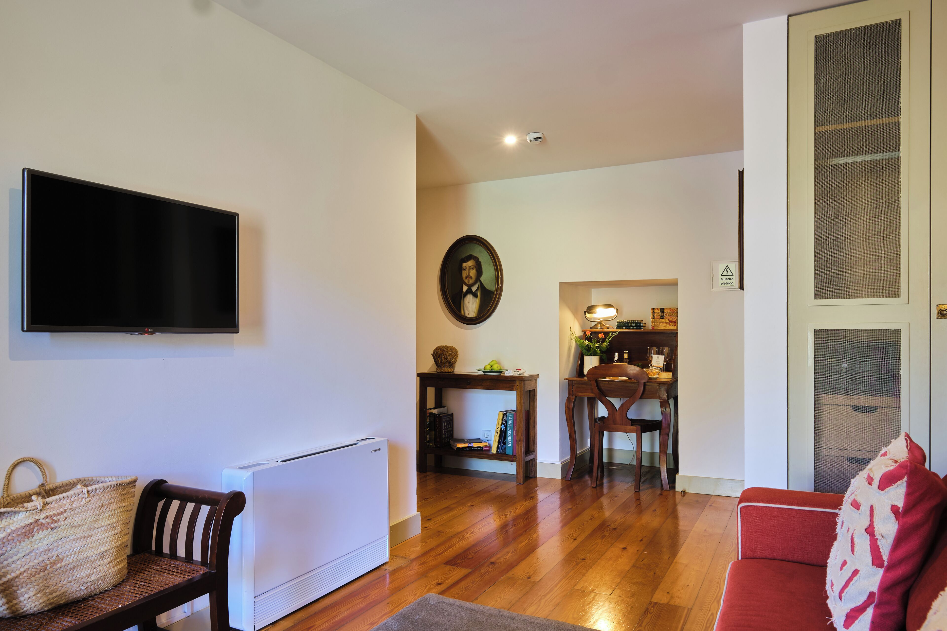 A living room with a flat-screen TV mounted on the wall, a sofa, a wooden chair, a dining table with chairs, and a radiator.