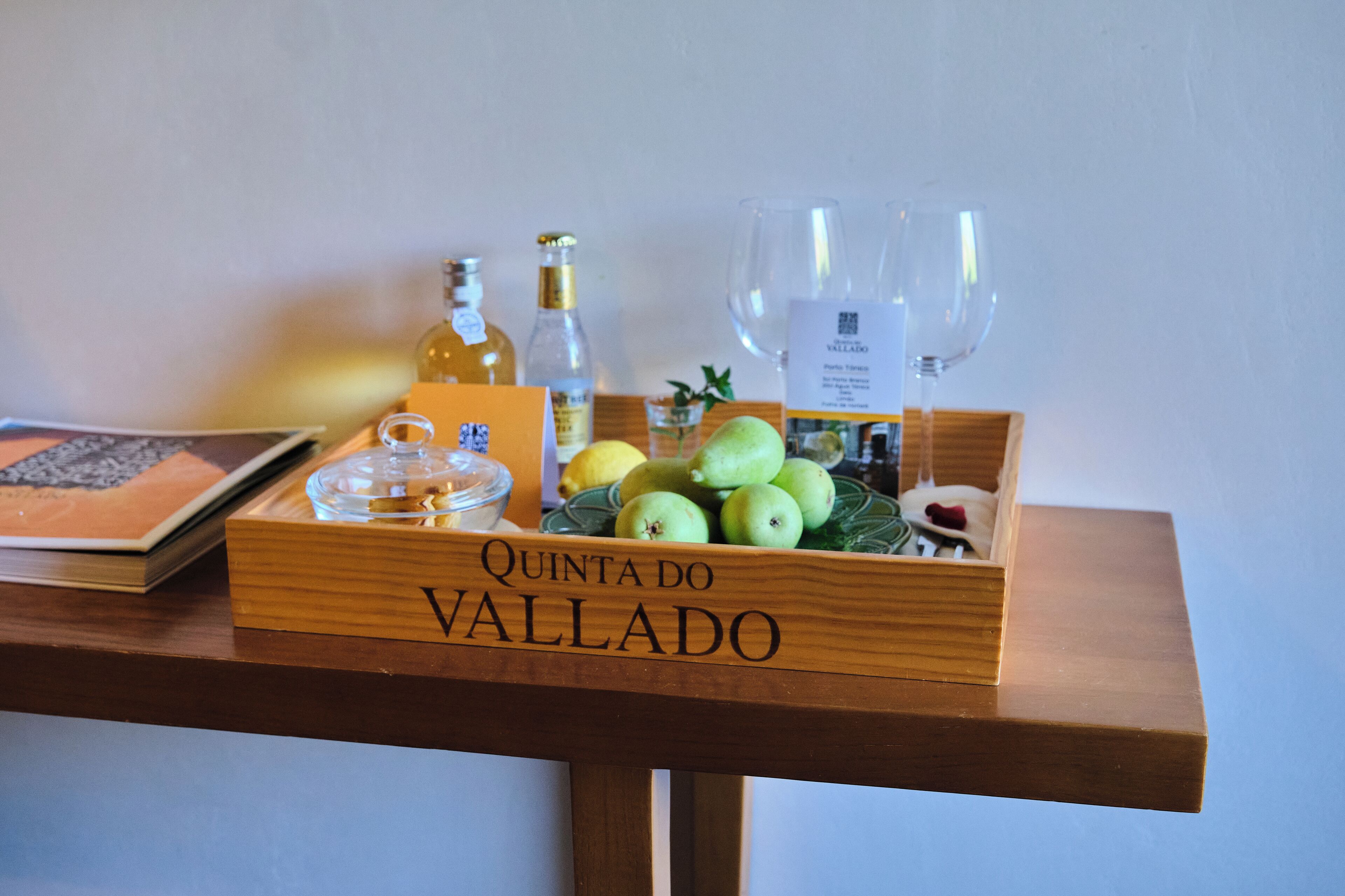 Een houten dienblad met de tekst 'Quinta do Vallado', met een keuze aan fruit, wijnflessen en glazen op een tafel.