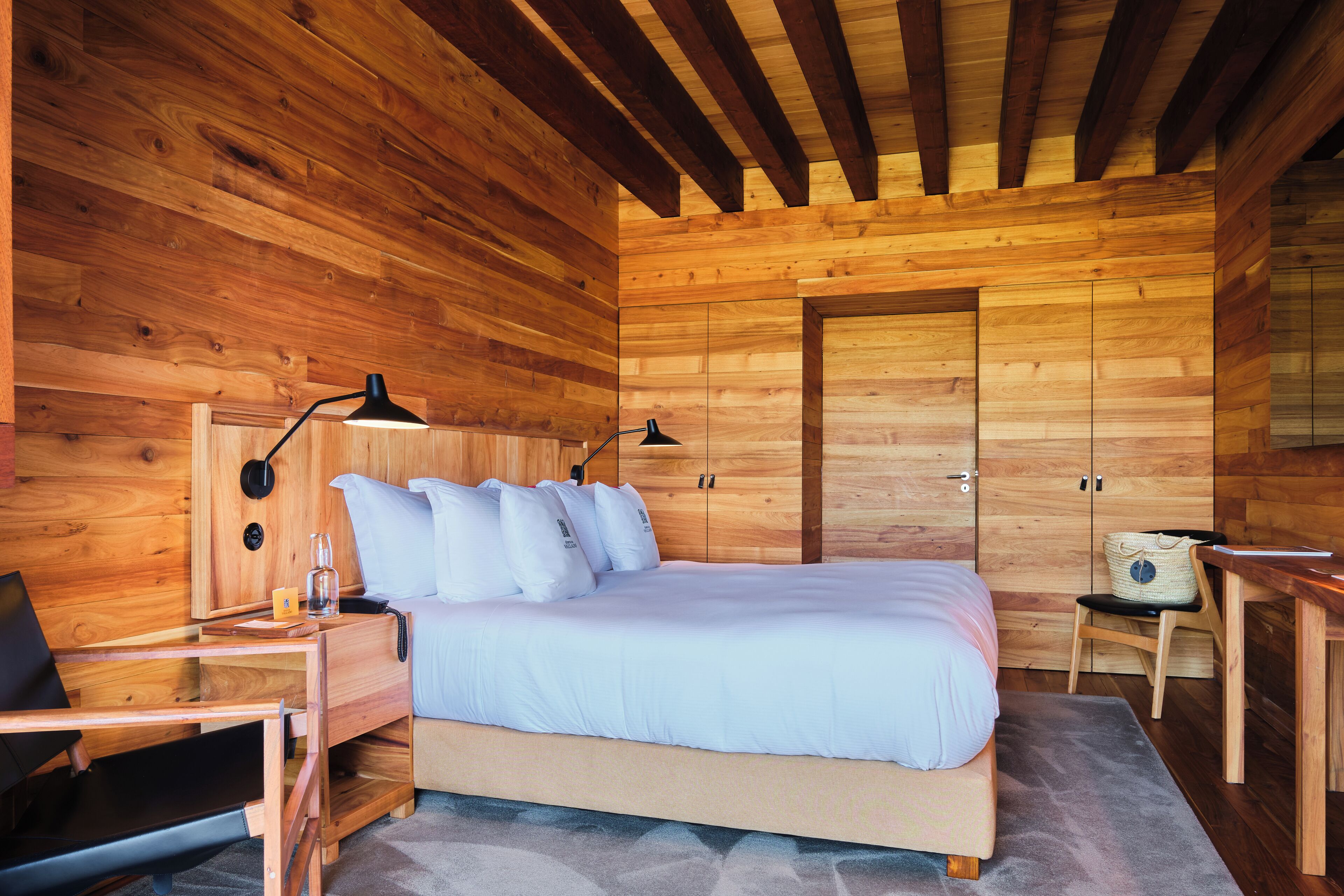 A wooden cabin bedroom with a bed, desk, chair, and a wardrobe.