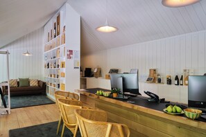 A reception area with a wooden reception desk, wicker chairs, a sofa, and a bookshelf with various items.