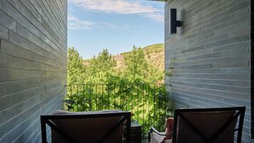 Un balcón con dos sillas, una mesa pequeña y vistas a un paisaje verde con árboles y colinas.