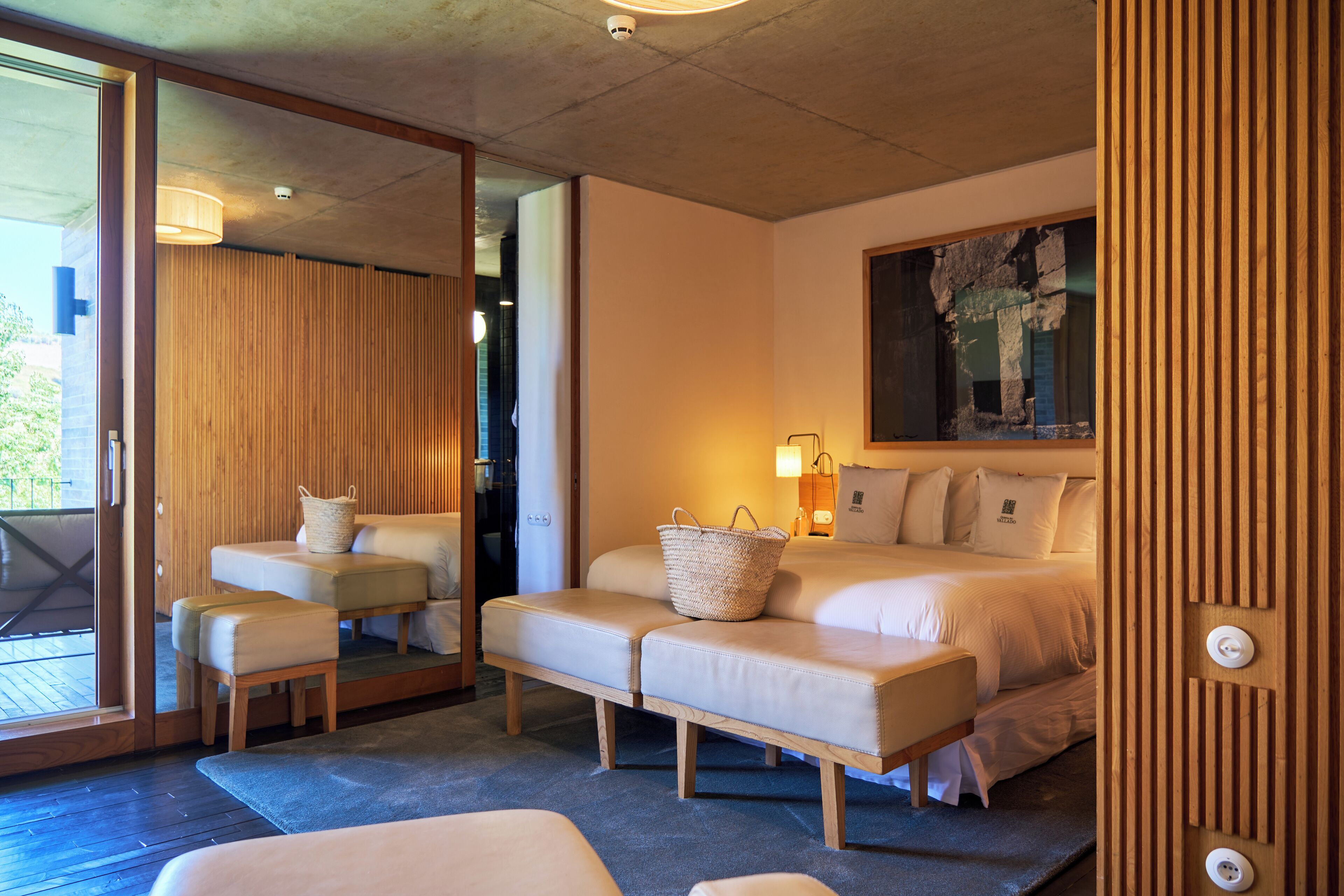 Una habitación de hotel moderna con una cama grande, un sofá, una mesita y un ventanal amplio.