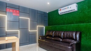 A modern lobby with a leather sofa, a wooden table, and a green accent wall. - Hotel Riva International - Near Nesco Center (Mumbai)