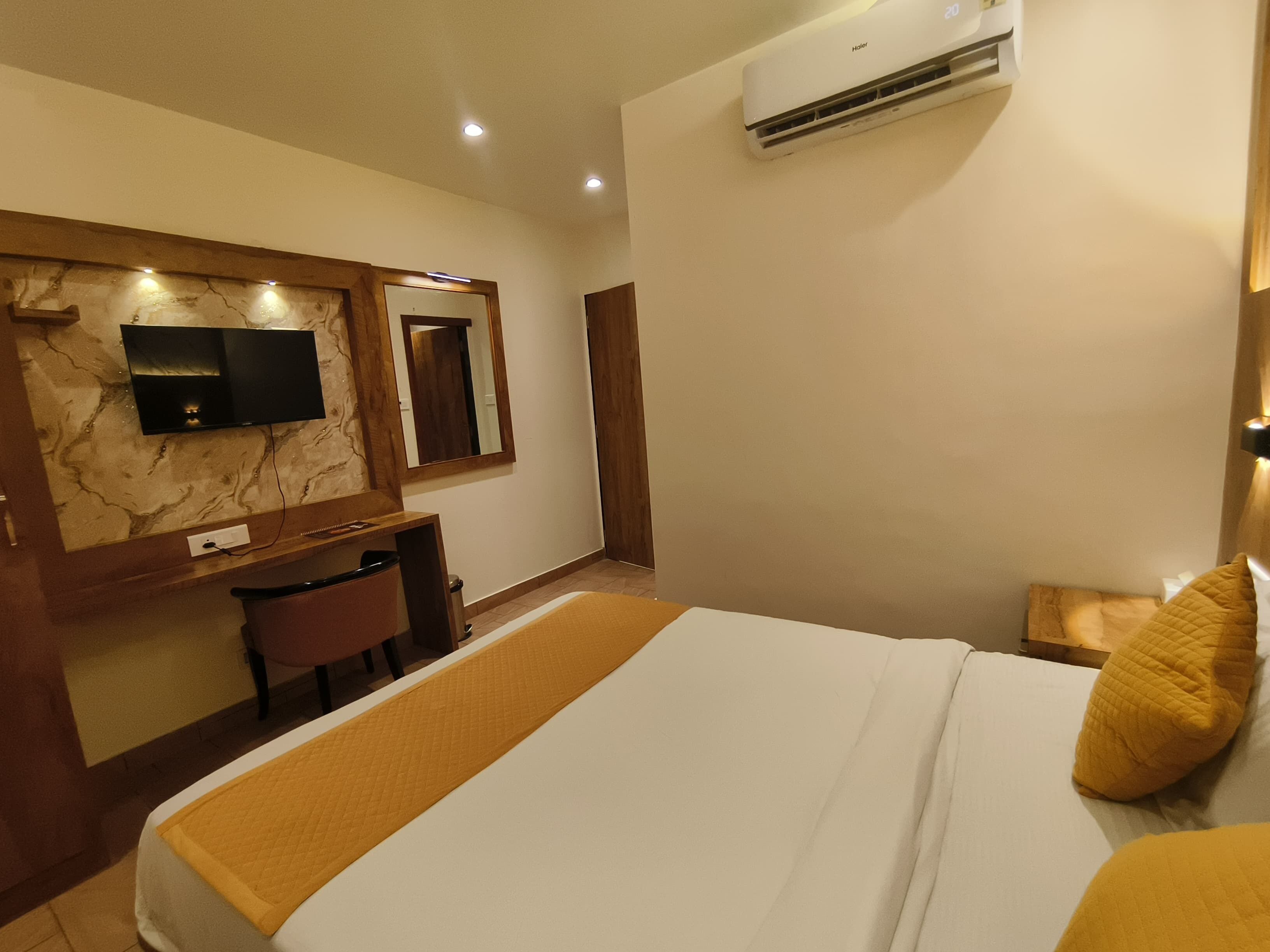 Ein Hotelzimmer mit Bett, Schreibtisch, Stuhl, einem an einer Marmorwand montierten Fernseher und einer Klimaanlage.