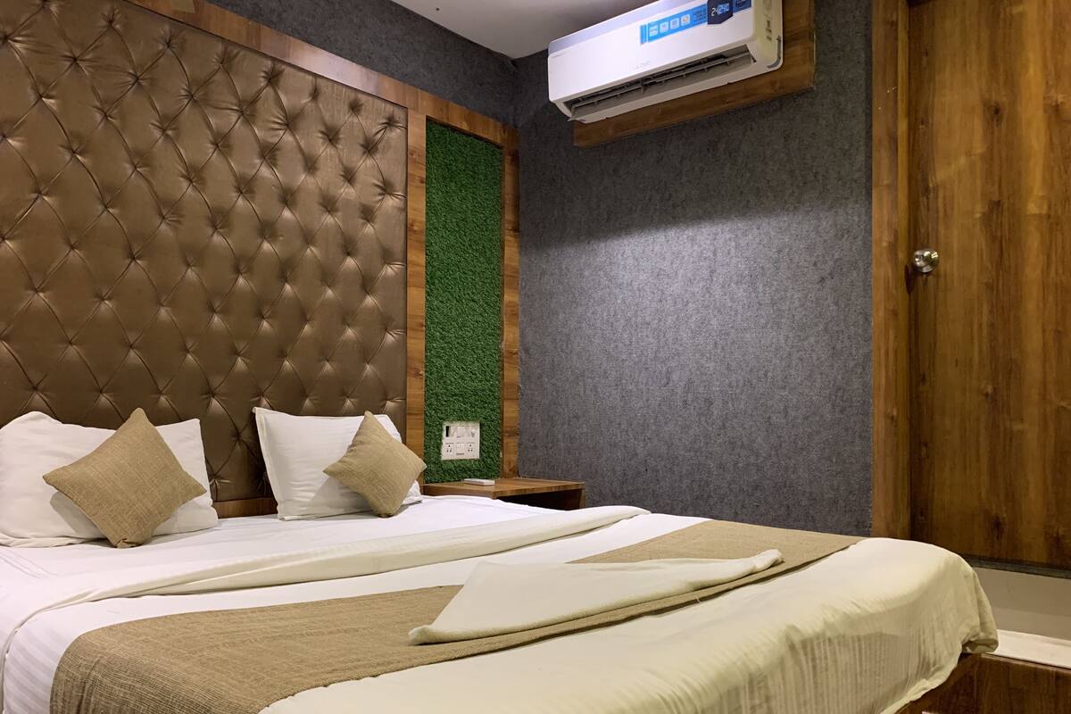 A hotel room with a tufted headboard, a green vertical accent wall, a wooden door, and an air conditioning unit.