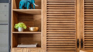 Un mueble de madera con estantes que contiene una escultura de ballena blanca, una figurita de elefante azul, una planta en maceta y un cuenco de latón.