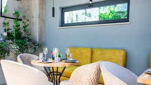Un comedor con una mesa redonda preparada para dos personas, un sofá amarillo y un ventanal con vistas a la vegetación.