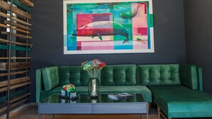 Un salón moderno con un sofá verde, una mesa de centro de cristal y un cuadro abstracto colorido en la pared.