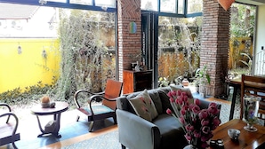 Un salón acogedor con un sofá, sillas y una mesa de centro. Hay plantas en macetas y un jarrón con flores sobre la mesa.