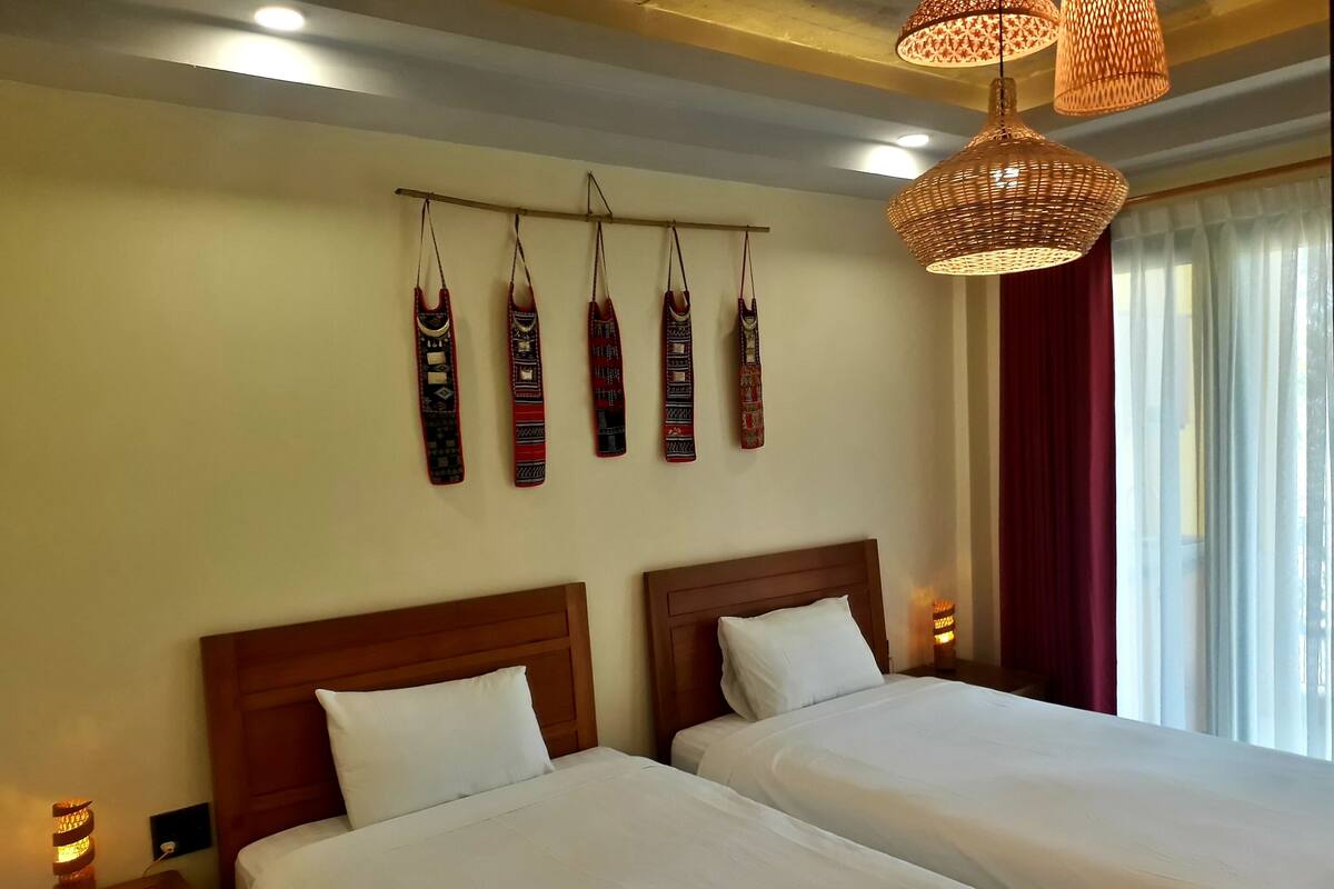 Une chambre d’hôtel avec deux lits, un luminaire fixé au mur et une fenêtre avec des rideaux.