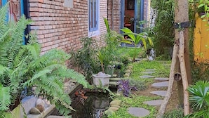 Un jardín con un muro de ladrillo, un estanque pequeño, piedras para pisar y abundante vegetación.