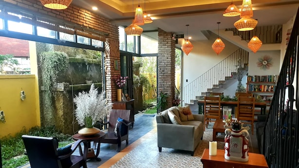 Una sala de estar moderna con un sofá, sillas y un comedor. Se ve una escalera que conduce a un nivel superior con una estantería.