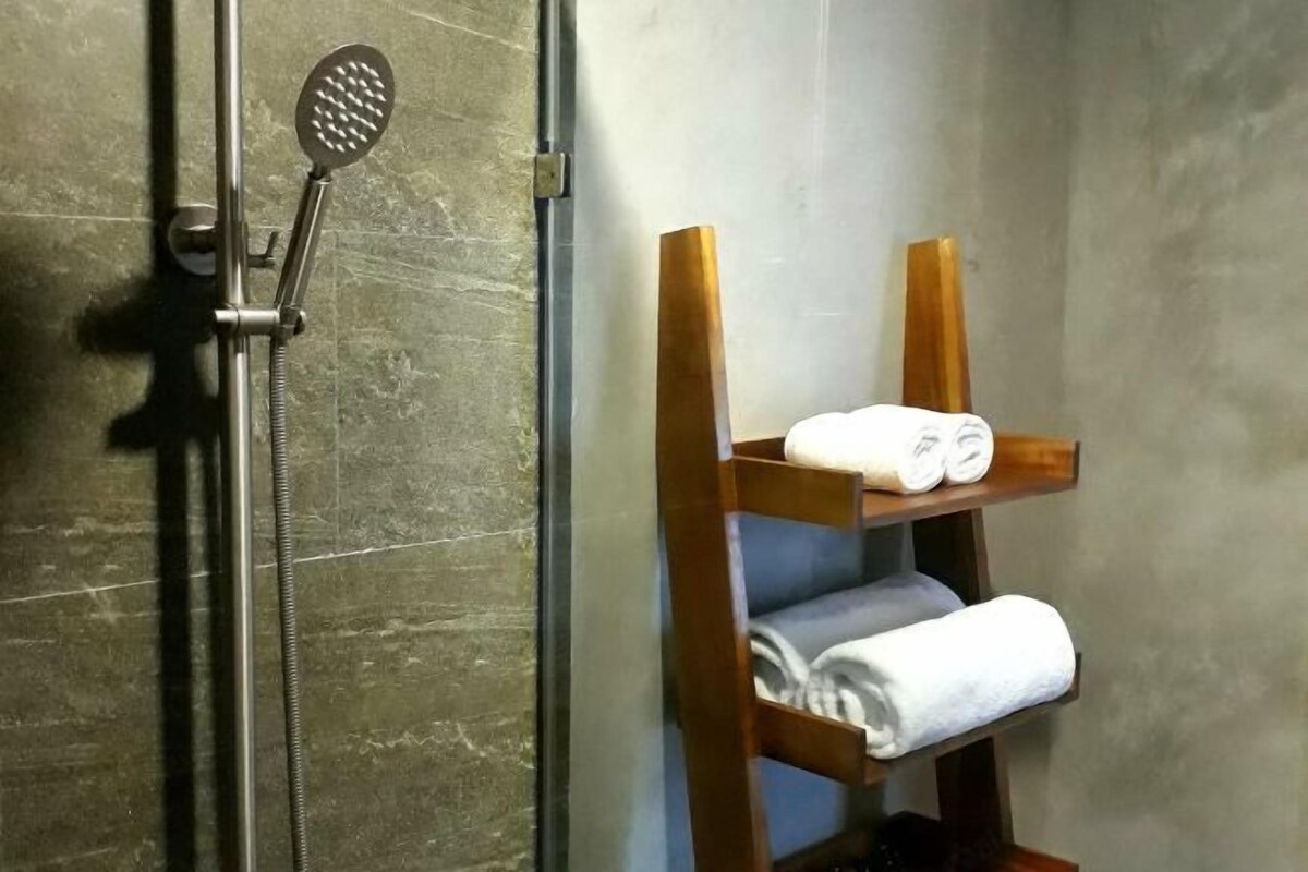 A bathroom with a shower, a towel rack with folded towels, and a wooden shelf.