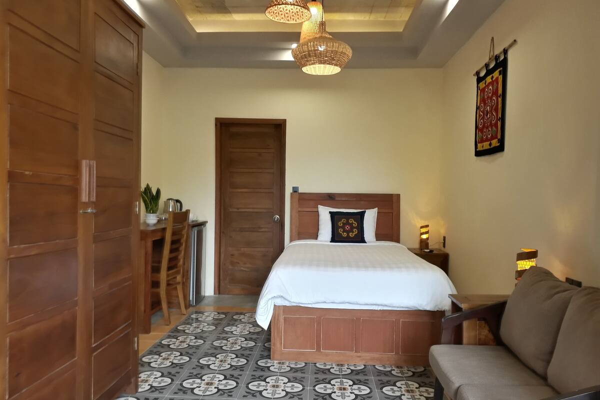 Une chambre à coucher comprenant un lit, un canapé, une armoire en bois, une table à manger avec des chaises et un sol à motifs.