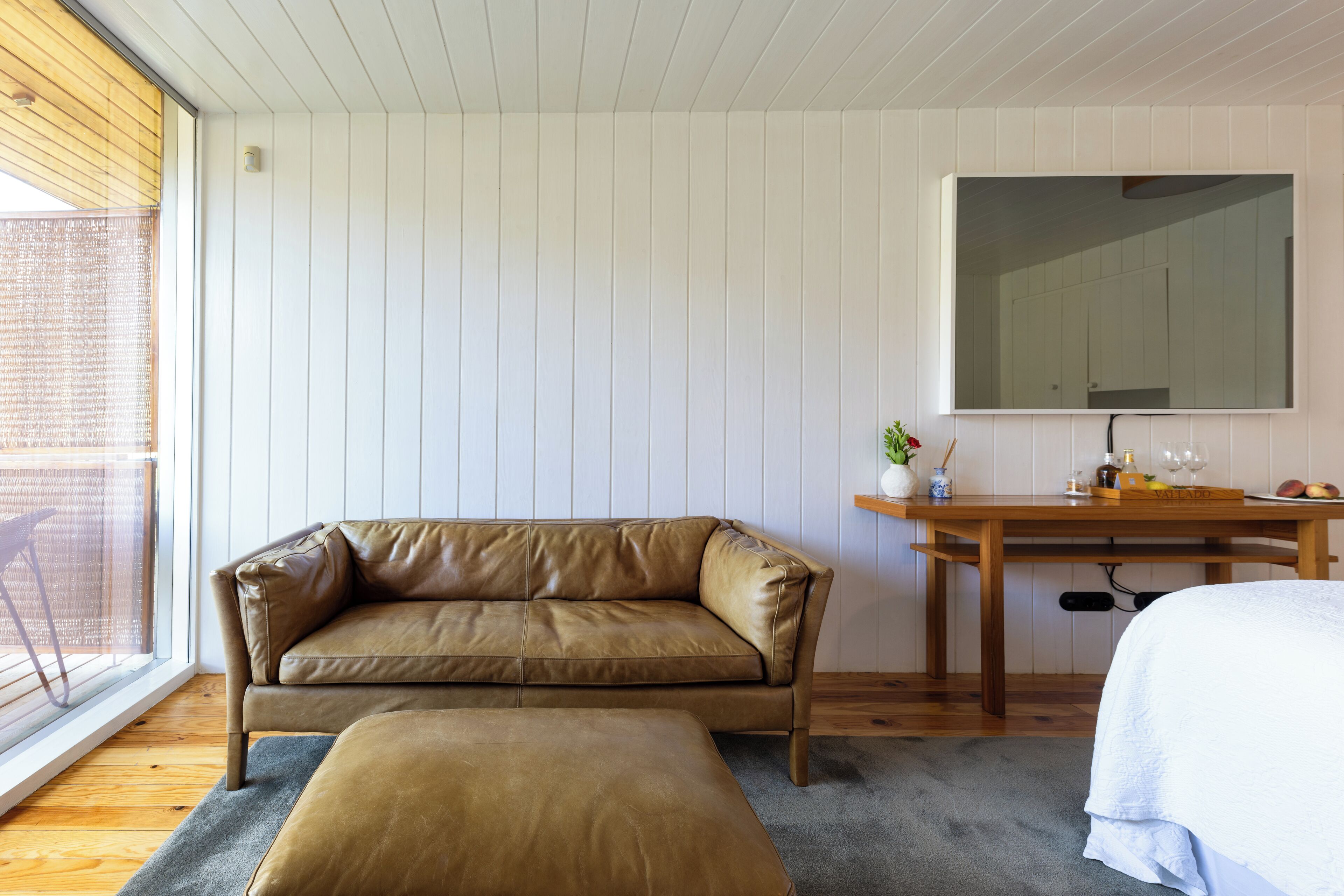 A room with a leather sofa, a wooden desk, a large mirror, and a window with a view.
