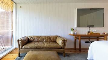 A room with a leather sofa, a wooden desk, a large mirror, and a window with a view.