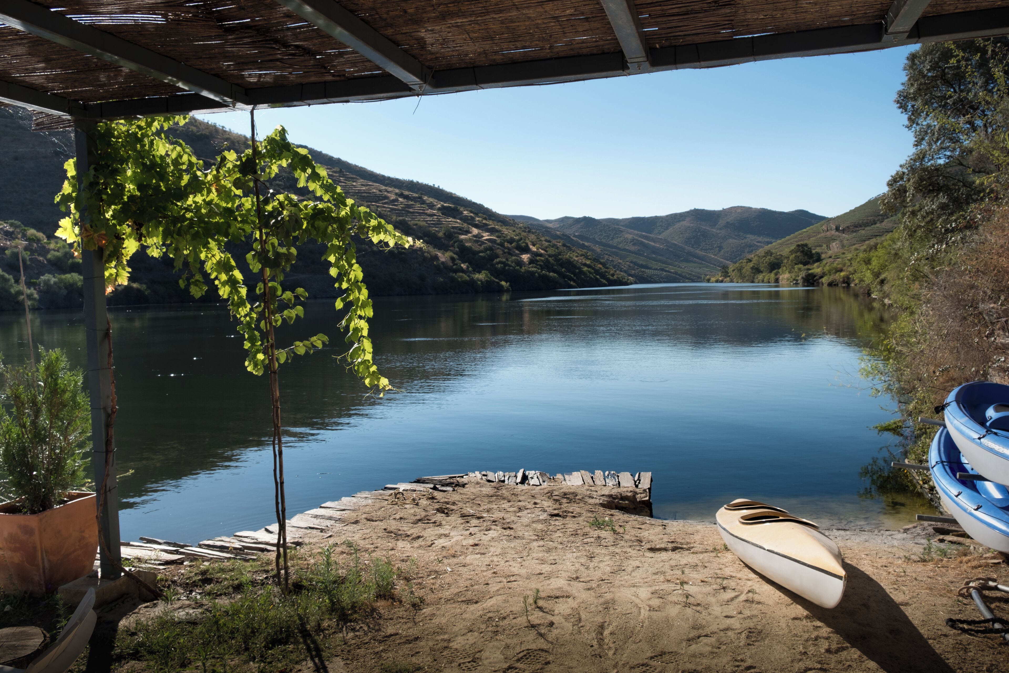 A covered dock with a canoe and a kayak, overlooking a calm lake with hills in the background.