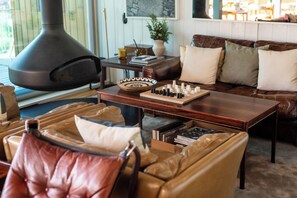 A cozy living room with a large fireplace, leather furniture, a chessboard, and a bookshelf.