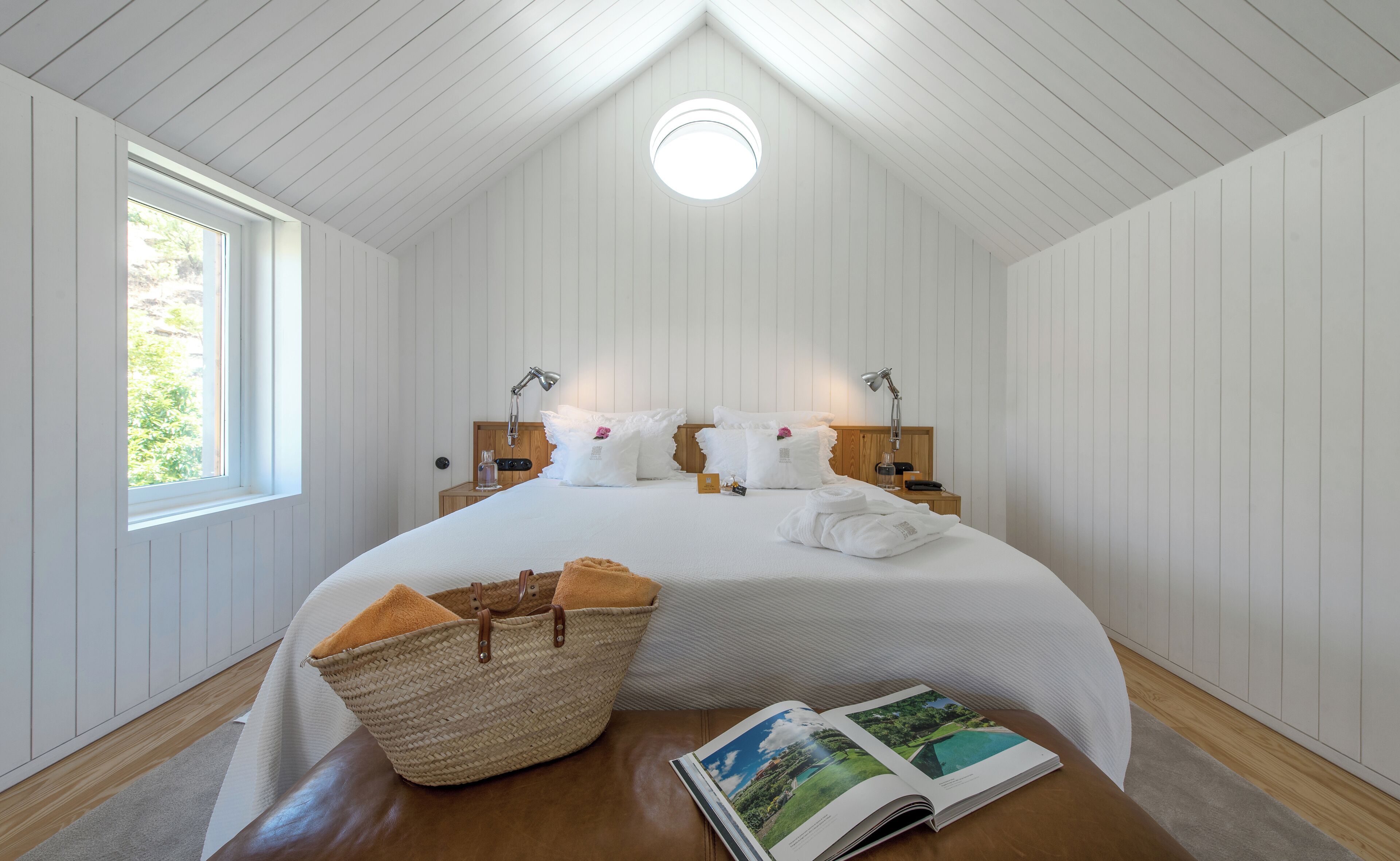 A bedroom with a large bed, two bedside tables, a window, a skylight, and a woven basket on the floor.