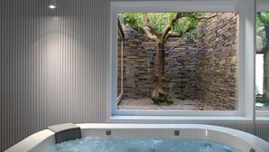Un área de spa con un jacuzzi, una pared de piedra y una ventana con vista a un árbol.