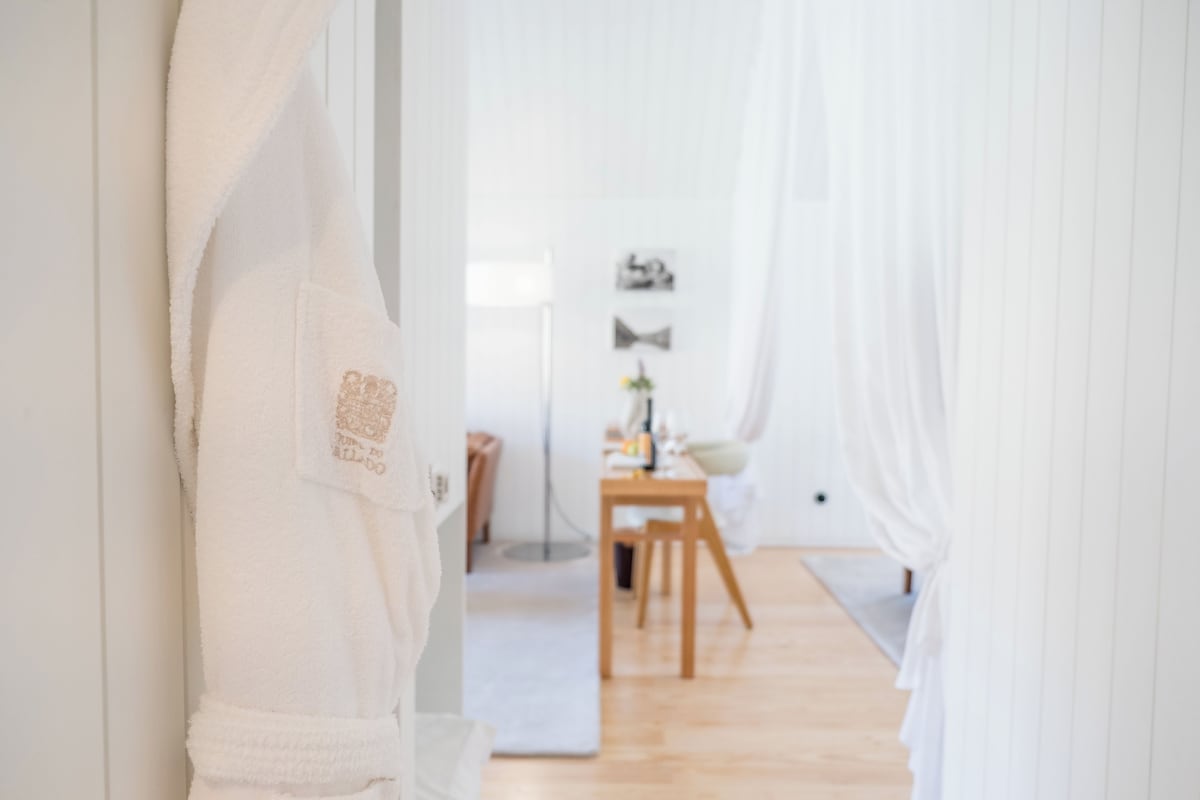 Un pasillo con una bata blanca colgada en una puerta, una zona de comedor con una mesa y sillas, y una planta pequeña sobre la mesa.