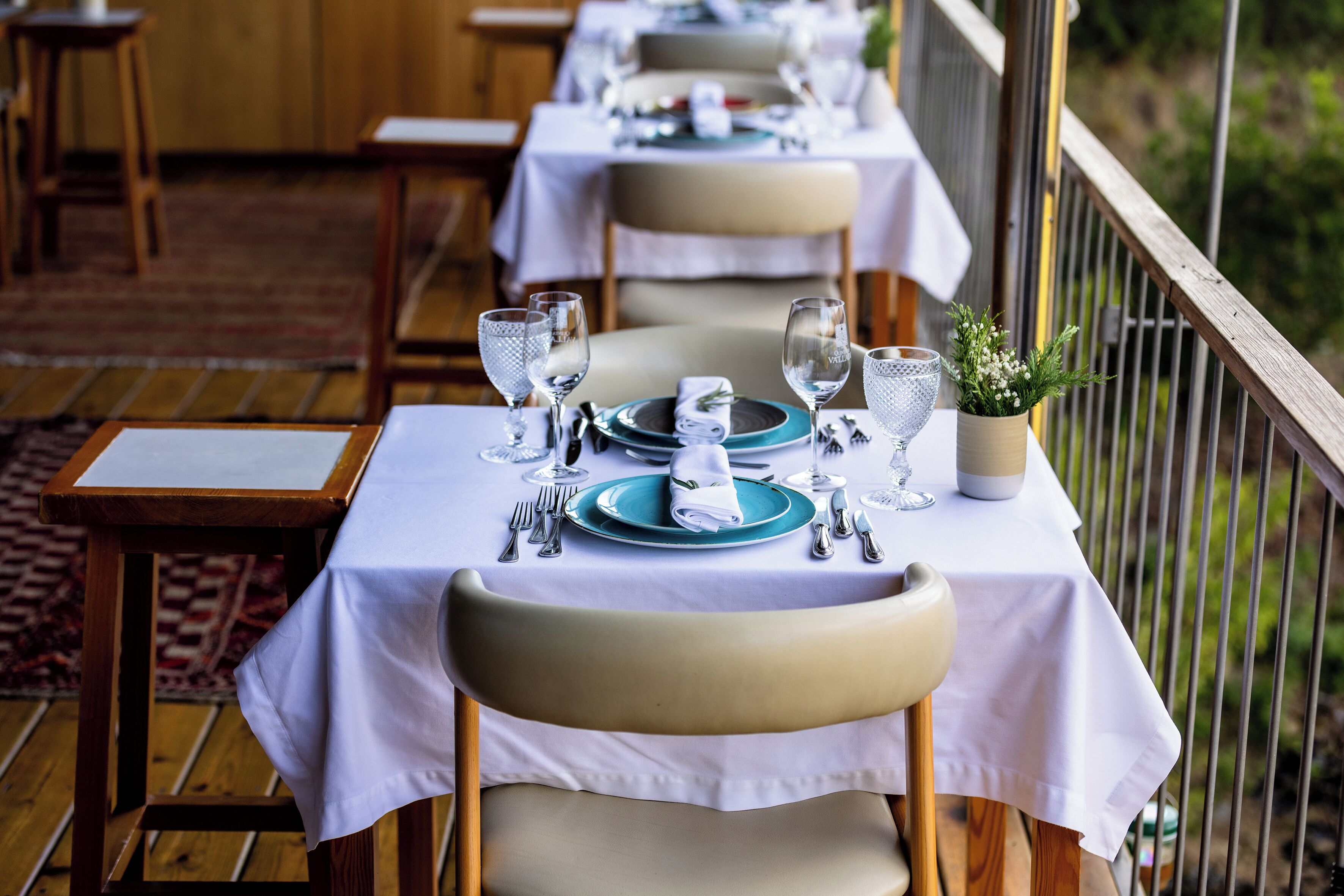 A dining area with tables set for two, each with a white tablecloth, blue plates, and silverware.