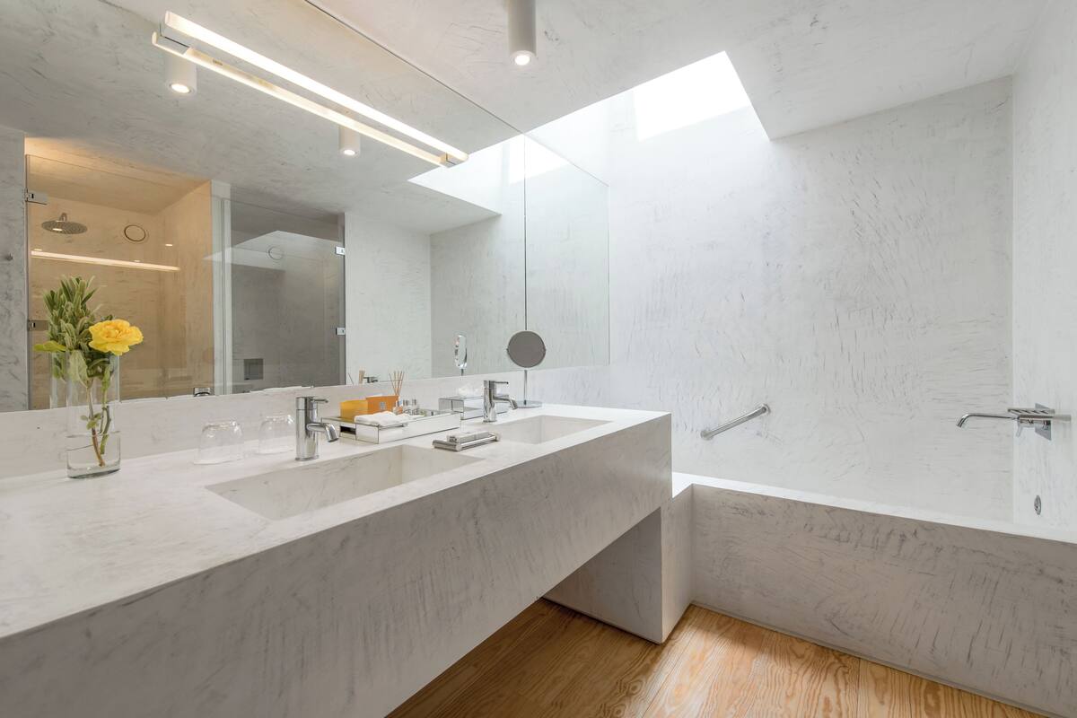 Un baño moderno con un espejo grande, dos lavamanos, una bañera y un tragaluz.
