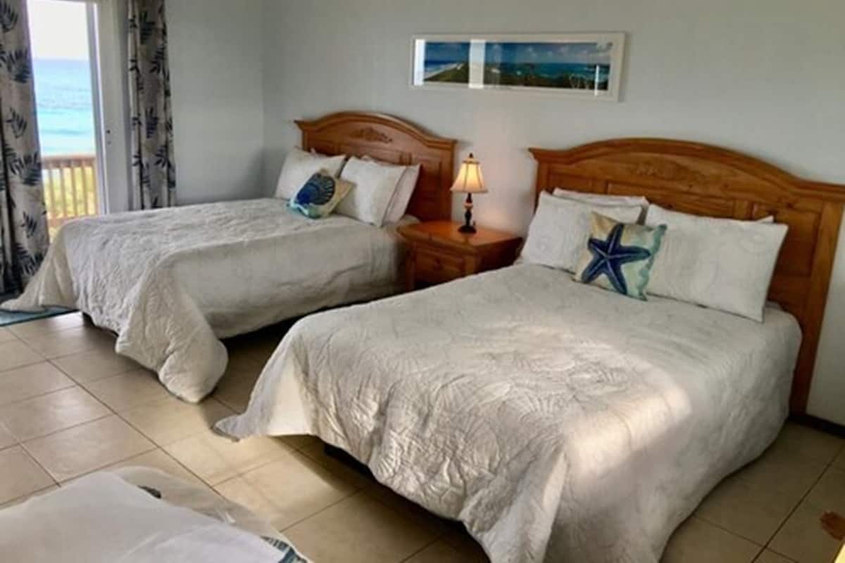 Una habitación con dos camas, una mesita de noche con lámpara y una ventana con cortinas.