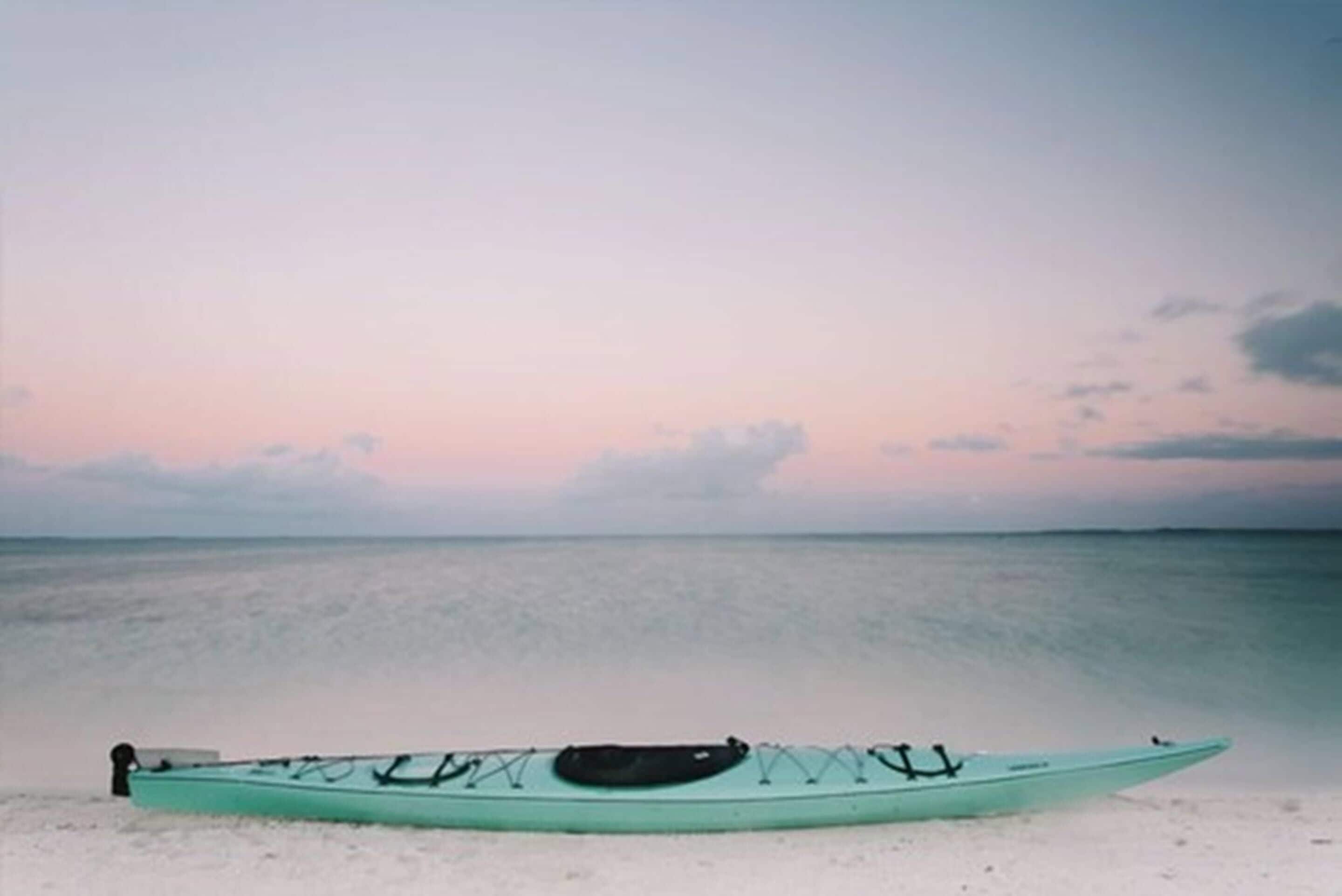 Un kayak sobre una playa arenosa, con mar tranquilo y cielo despejado.